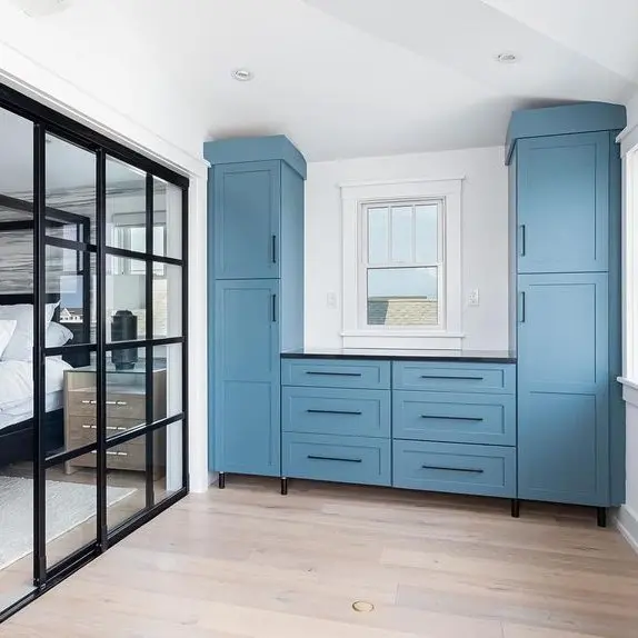Blue built-in cabinetry flanking a window with a dark countertop, beside a black-framed glass partition