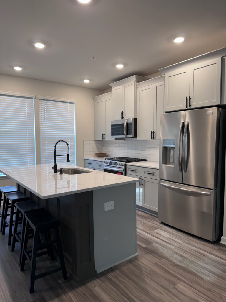 White shaker kitchen with a large quartz-topped island, stainless refrigerator and black gooseneck faucet