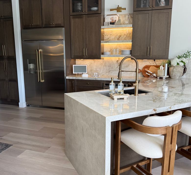 Dark wood Fabuwood kitchen with a waterfall quartz peninsula and brass faucet