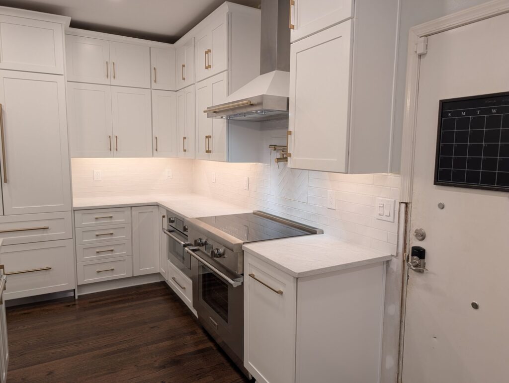 Cooktop and range with white herringbone tile backsplash, brass bar pulls and a deep drawer stack.