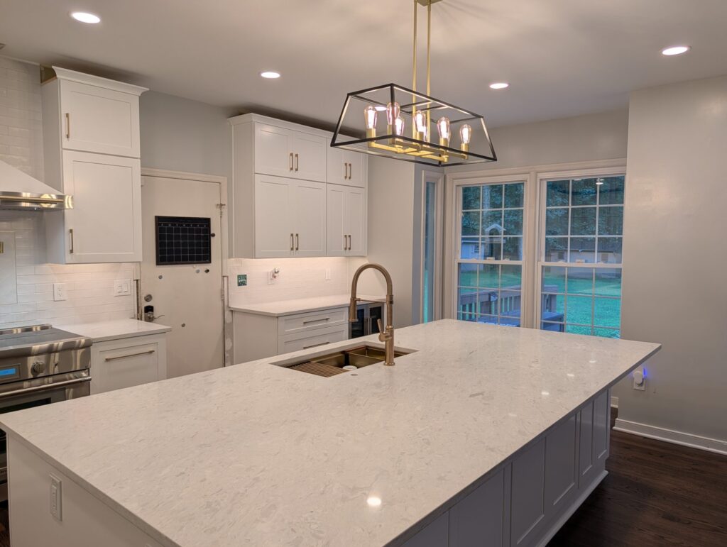 The finished kitchen — quartz island, brass fixtures and a black-and-brass linear lantern overhead.