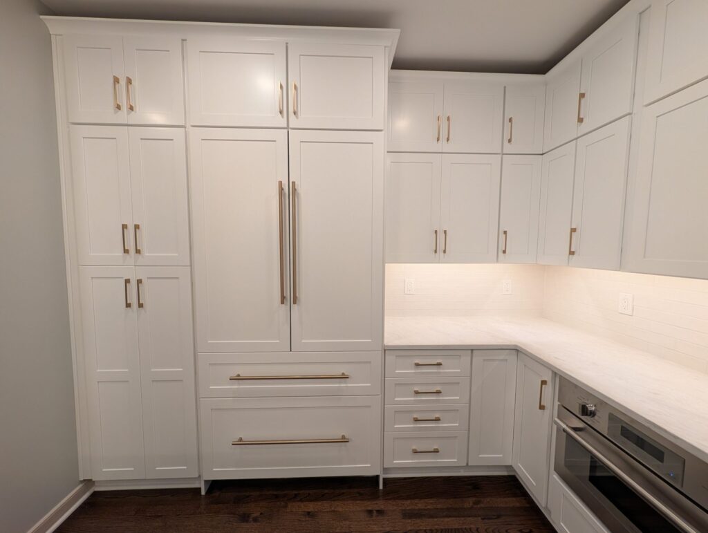 Floor-to-ceiling white shaker pantry cabinets and a panel-fronted refrigerator with brass appliance pulls.