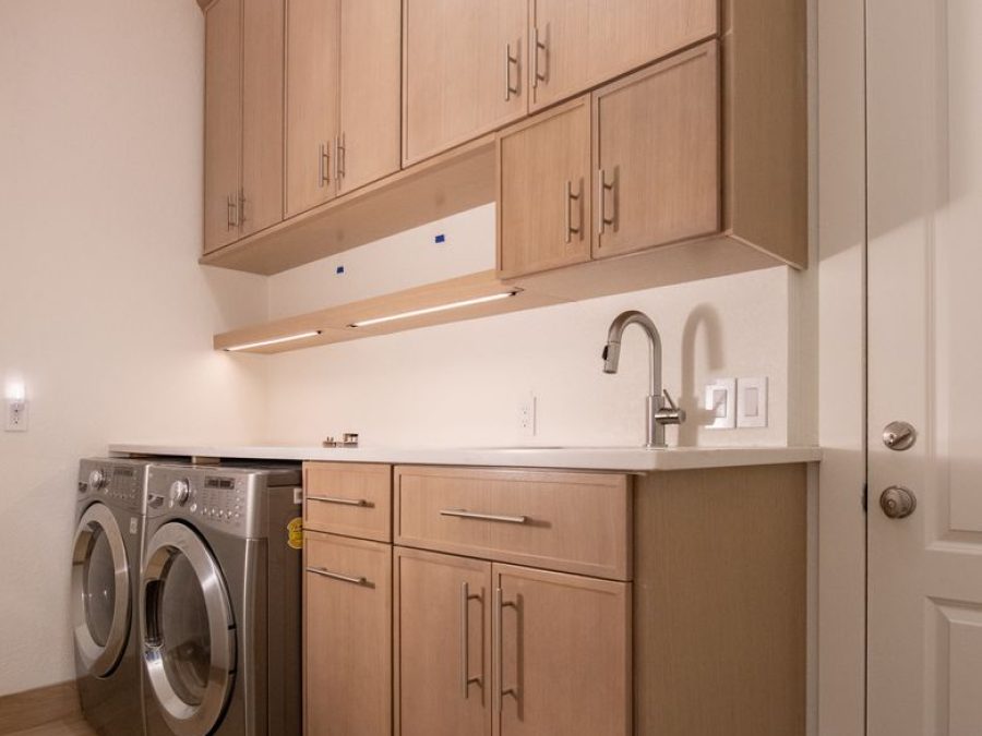 Laundry room with light natural-wood cabinets, under-cabinet lighting, a sink and front-load washer and dryer